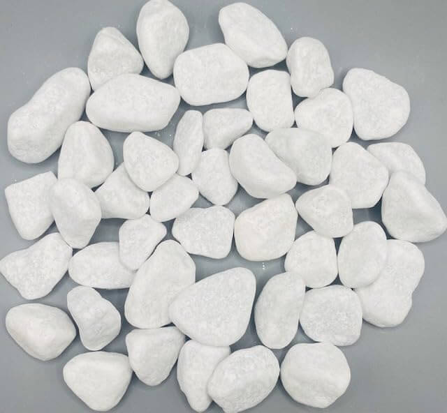 Schneeweiß Dekosteine I Marmorkies I Körnung 15-25mm I 1kg auf grauem Hintergrund, ideales Deko-Element für Kunstpflanzen.